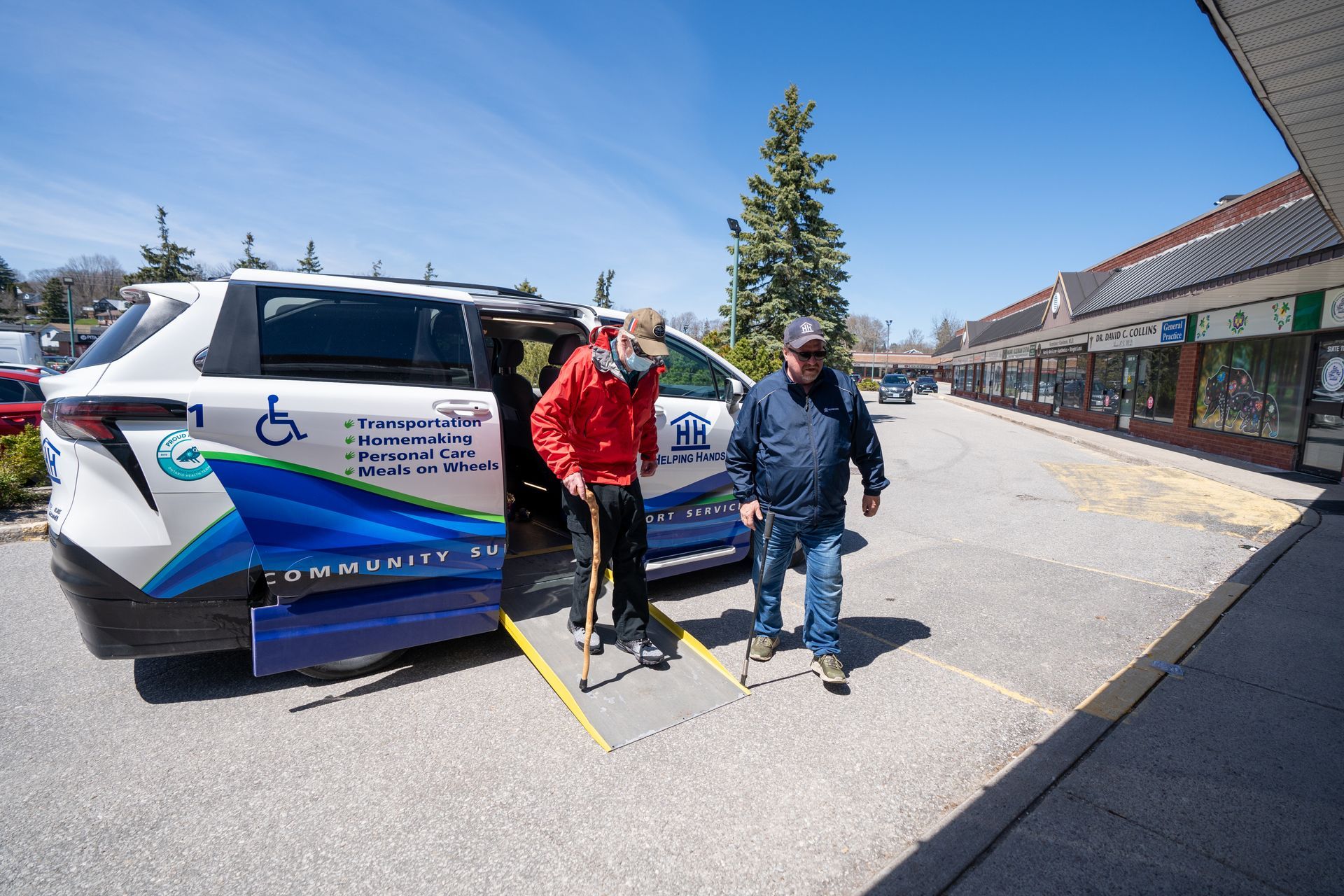 Two men are helping an elderly man get out of an assisted transportation vehicle.