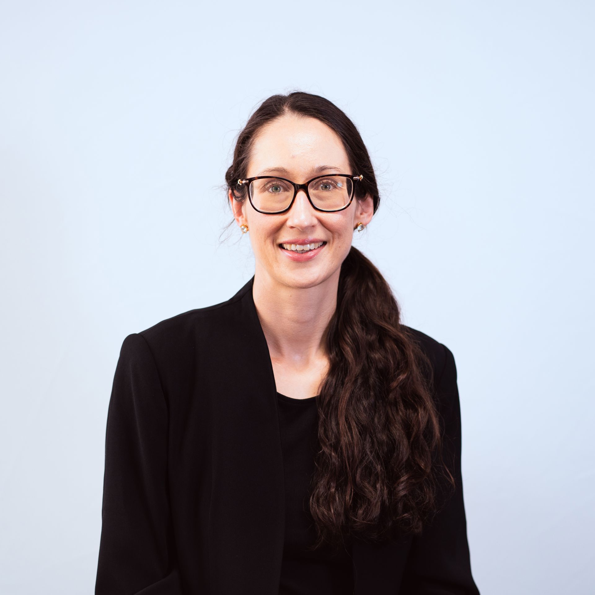 A woman wearing glasses and a black jacket is smiling for the camera.