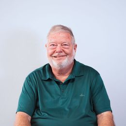 A man with a beard is wearing a green shirt and smiling.