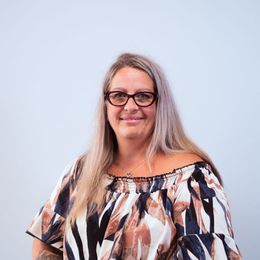 A woman wearing glasses and a patterned print shirt is smiling for the camera.