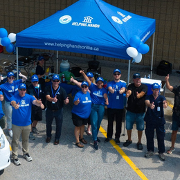 A group of people standing under a blue tent that says helping hands