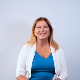 A woman in a blue dress and white cardigan is smiling for the camera.