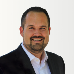 A man in a green striped shirt is standing in front of a white wall.