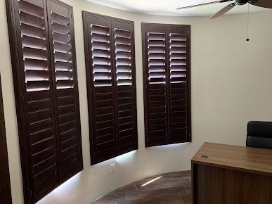 Dark brown shutters on curved windows in a room with a desk.