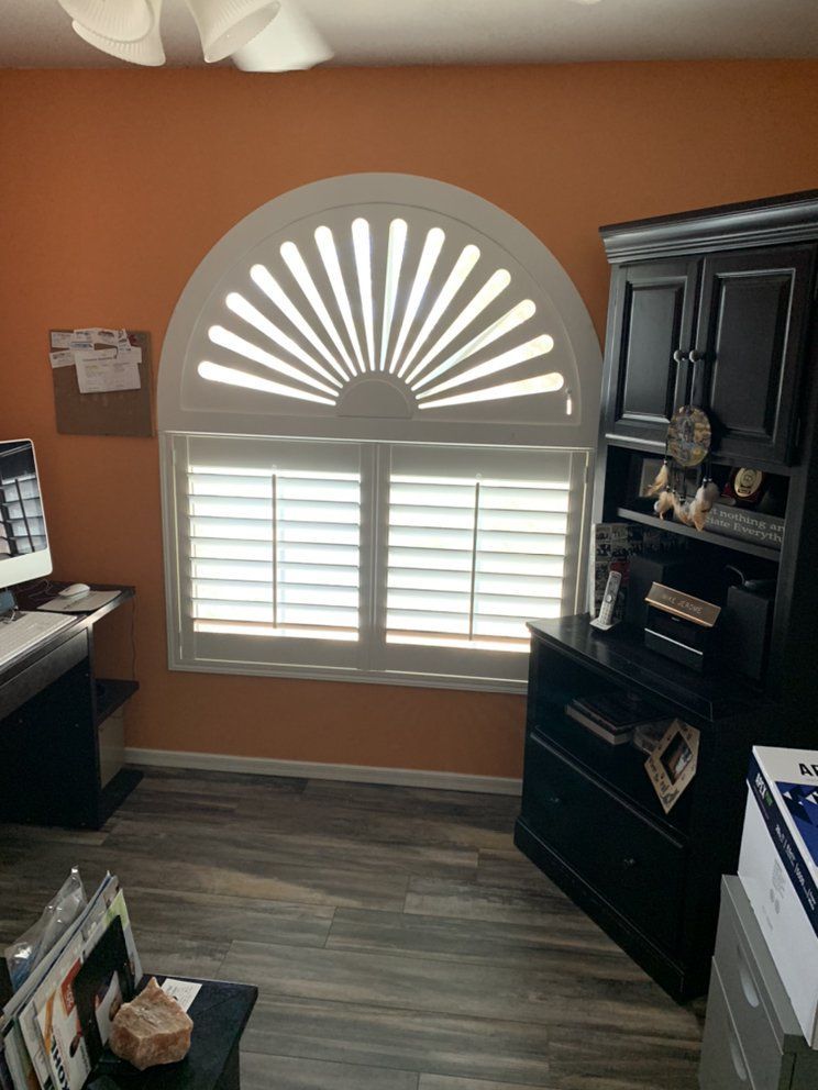 Office with an arched window featuring white shutters, orange walls, and a black cabinet.