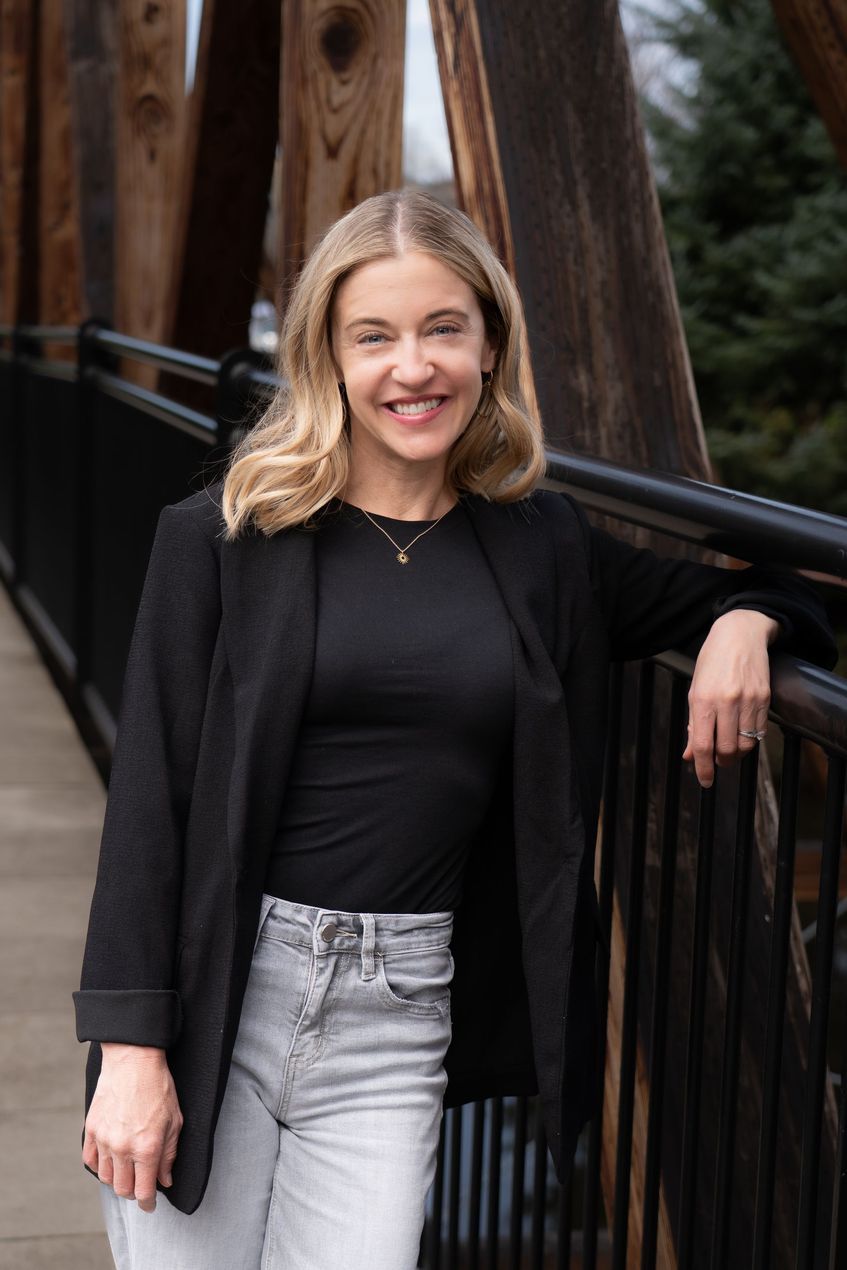 Sarah Newton poses in nature wearing a black shirt and a friendly smile.