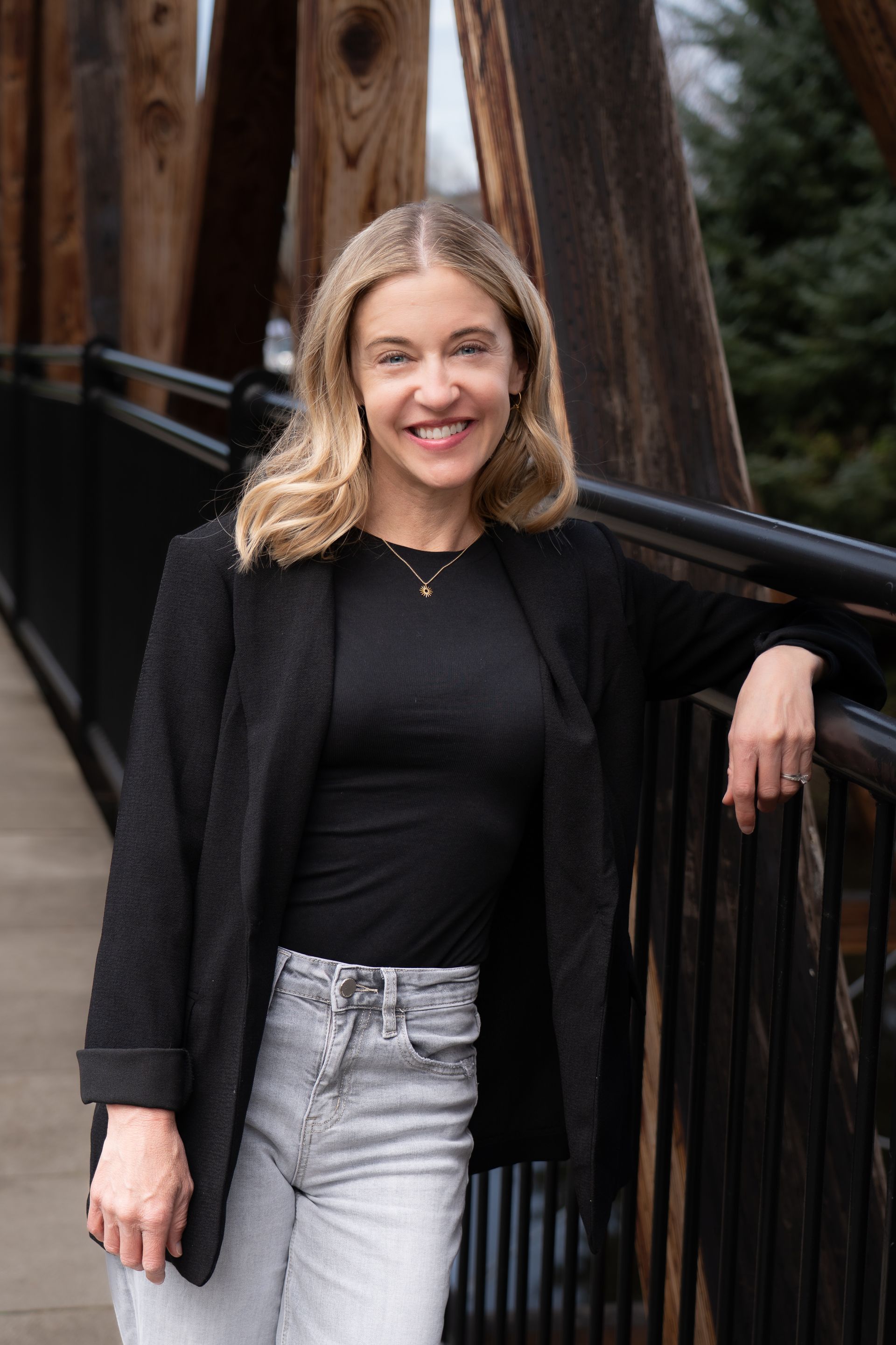 Sarah Newton poses in nature wearing a black shirt and a friendly smile.