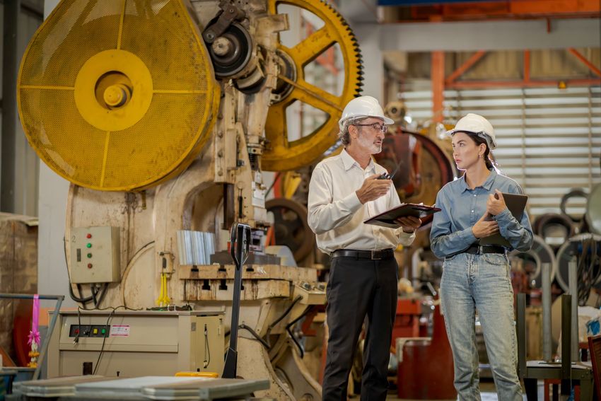 A man and a woman in hard hats have a conversation in a sheet metal factory