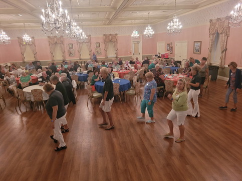 A large room filled with people sitting at tables and dancing.