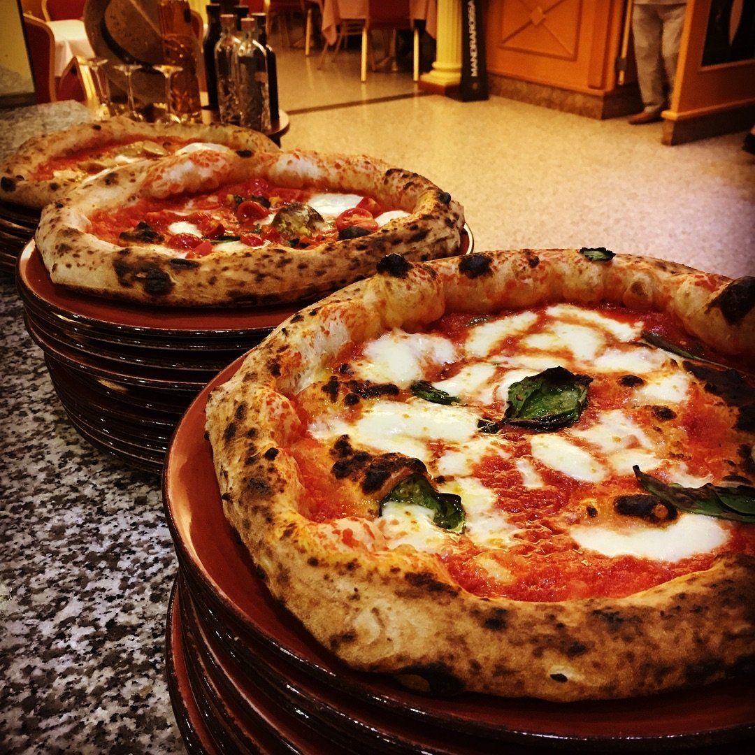 Pizze su piatti impilati con croste bruciacchiate, mozzarella, salsa di pomodoro e basilico, all'interno di un ristorante.