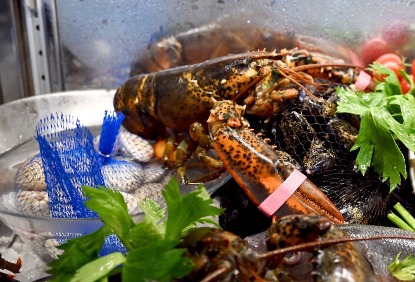 Esposizione di aragoste e altri frutti di mare con verdure e vongole in un ambiente da mercato del pesce.