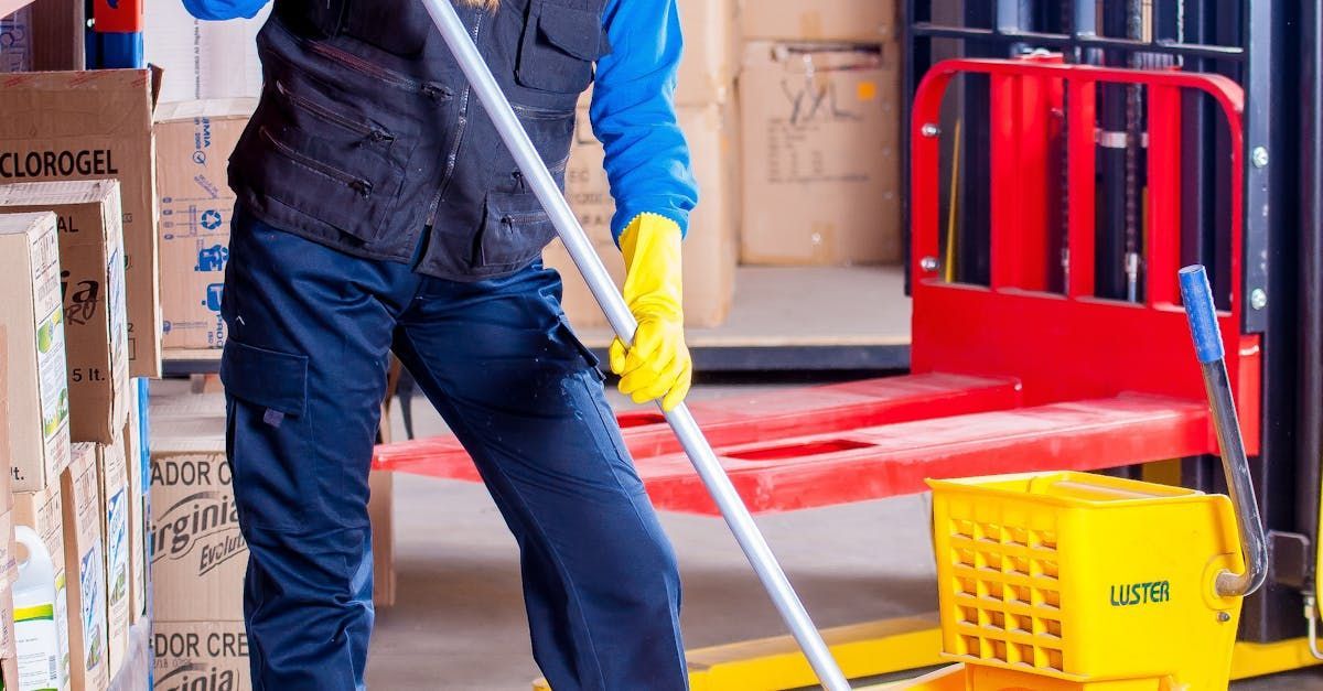 A man is cleaning the floor with a mop in a warehouse.