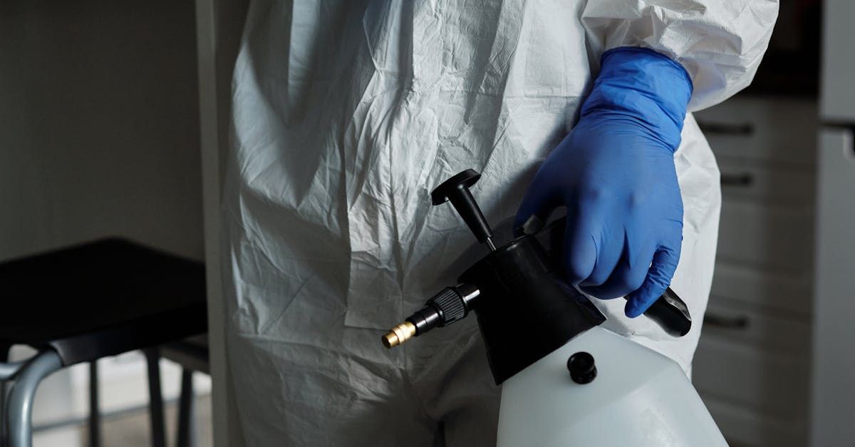 A person in a protective suit and blue gloves is holding a spray bottle.