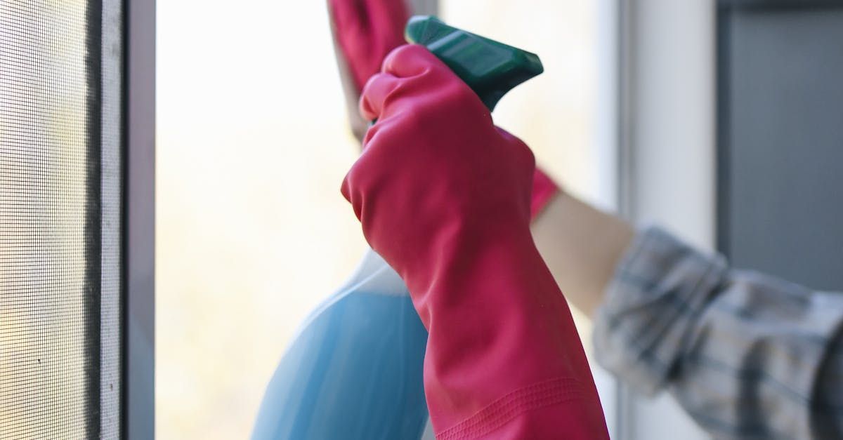 A person wearing red gloves is cleaning a window with a spray bottle.