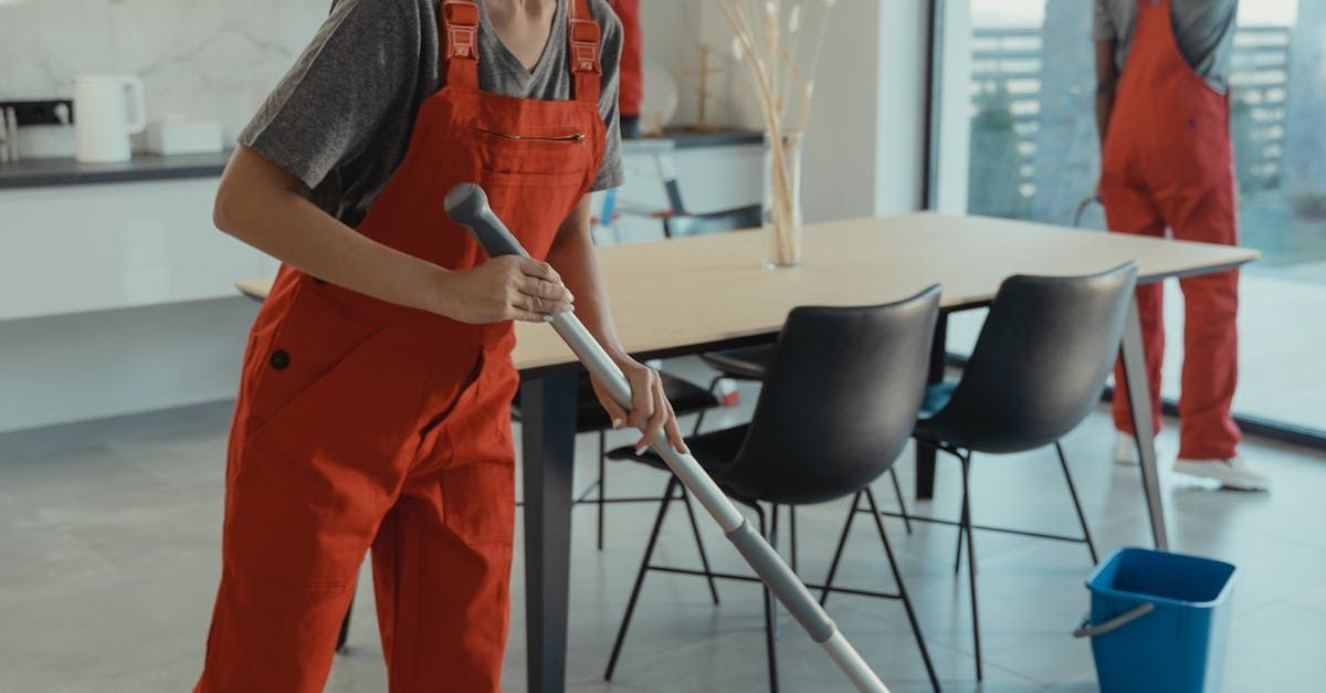 A man in red overalls is mopping the floor in a living room.