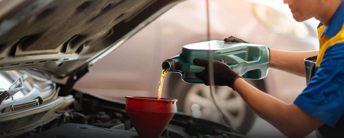 Mechanic pouring oil into a funnel in a car engine.| Super Express Lube