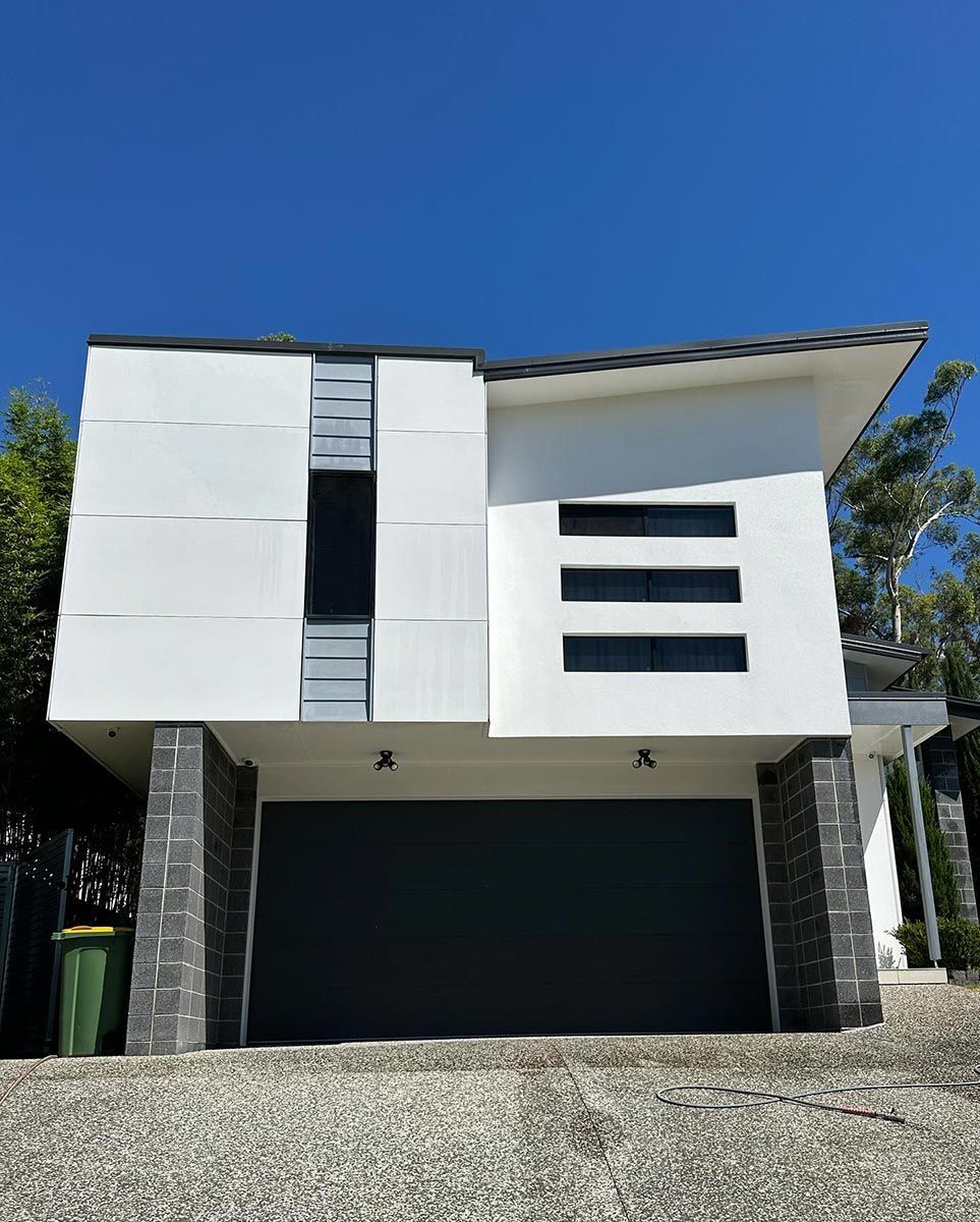 A White House With A Black Garage Door And A Blue Sky In The Background — Clean Cartel Pressure Washing In Reedy Creek, QLD