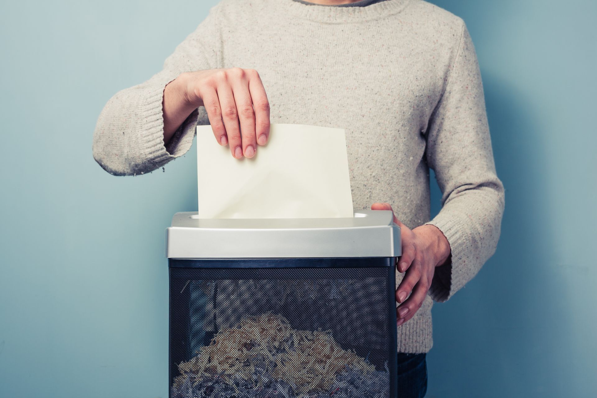 A person is putting a piece of paper in a paper shredder.