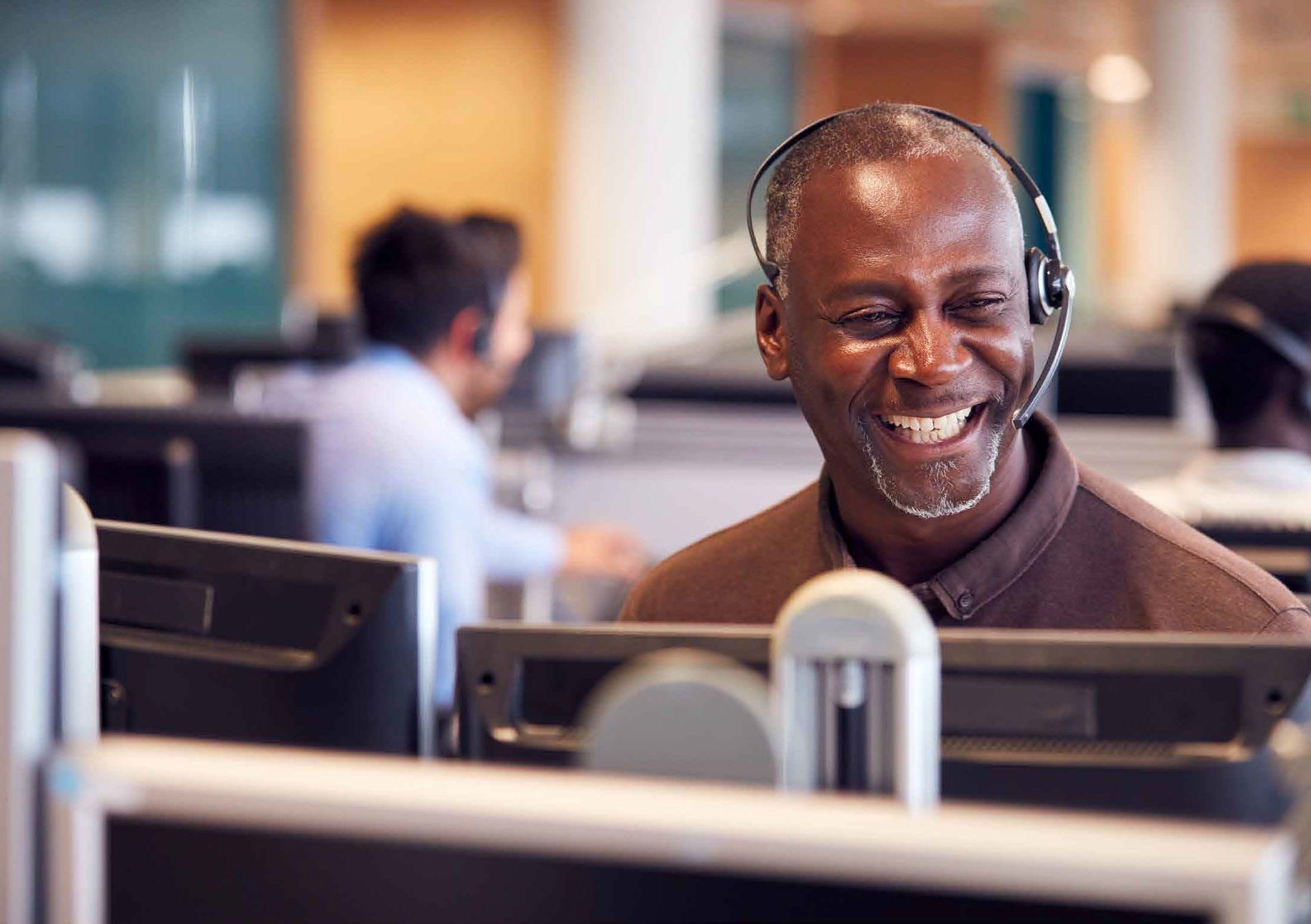 A man wearing a headset is sitting in front of a computer in an office.