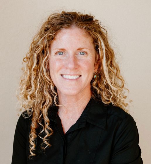 A woman with curly hair is smiling and wearing a black shirt