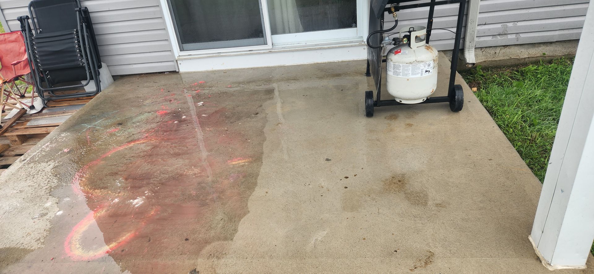 Un réservoir de propane est posé sur un patio en béton à côté d'une porte coulissante en verre.