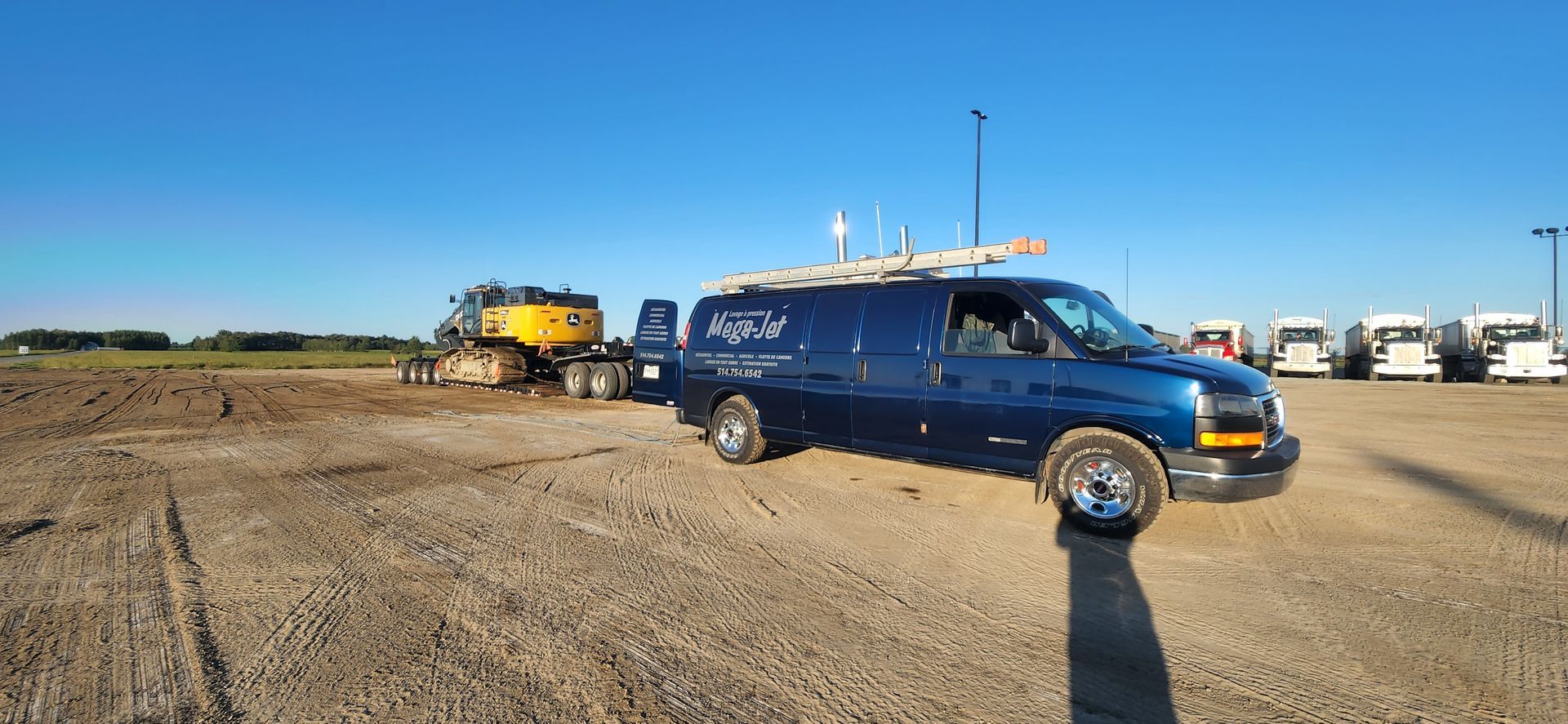 Une camionnette bleue avec une échelle dessus est garée sur un terrain en gravier.