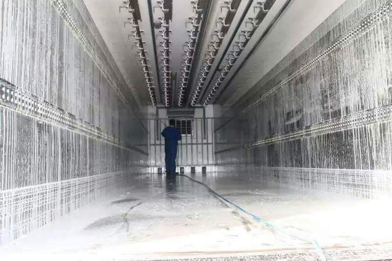 Un homme nettoie l'intérieur d'une remorque réfrigérée.