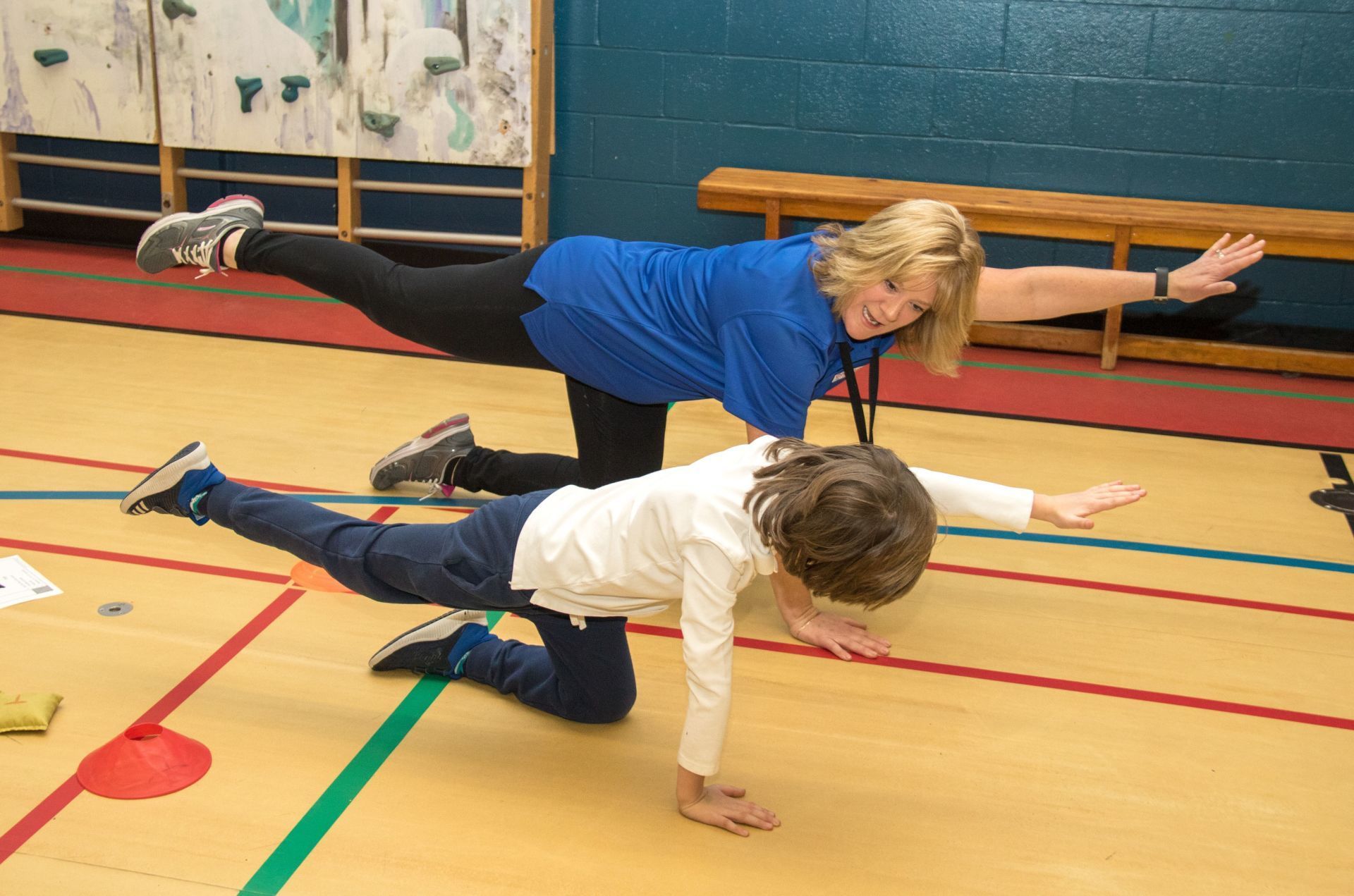 A woman in a blue shirt is helping a child do a balance exercise