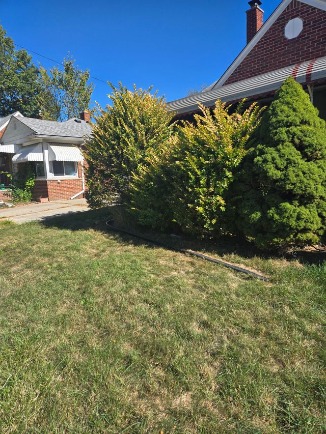 A brick house with a front porch, surrounded by lush green bushes and trees under a clear blue sky.