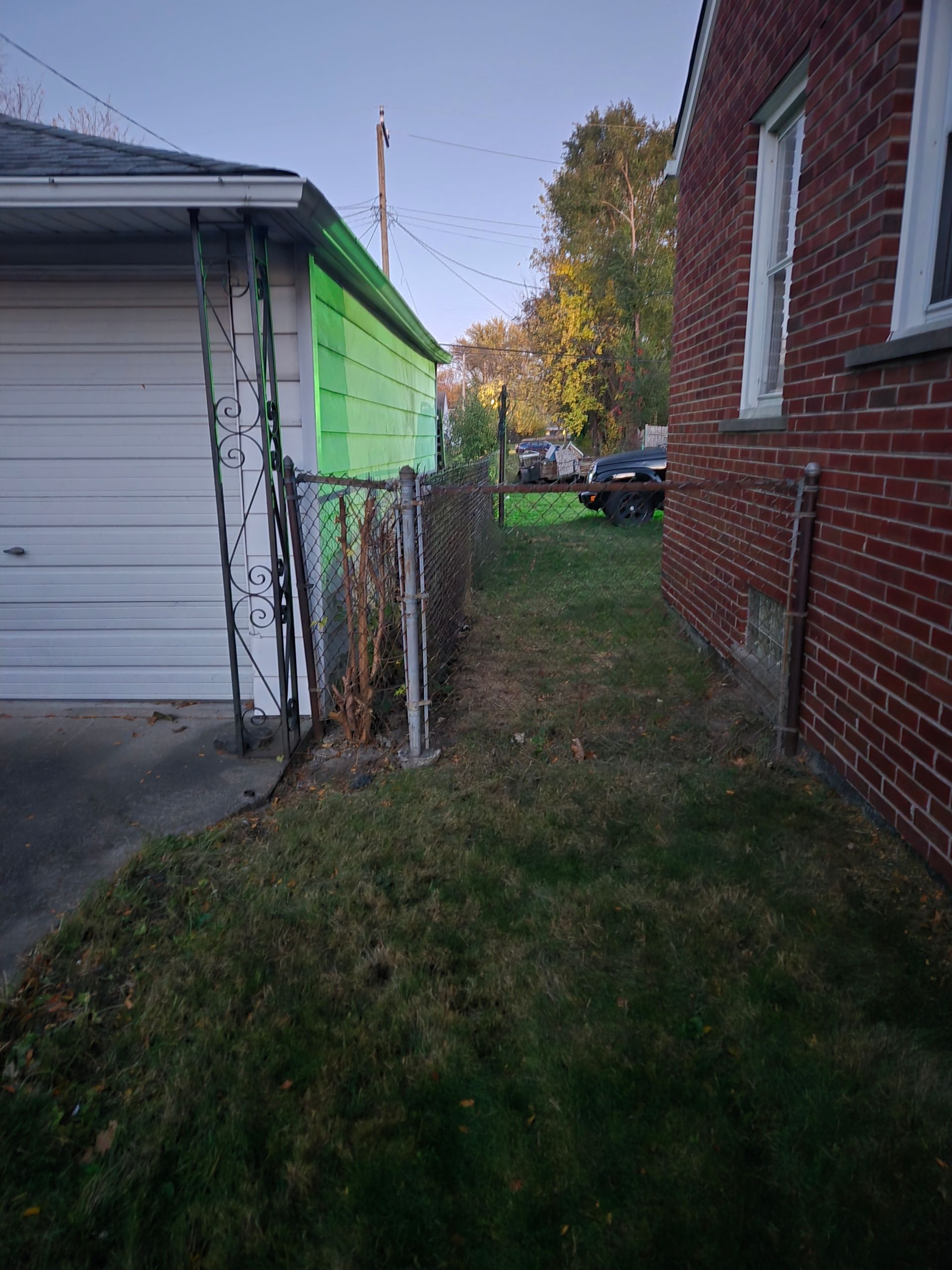 A side view of a residential yard showing a garage with neon green siding, a chain-link fence, and a brick house.