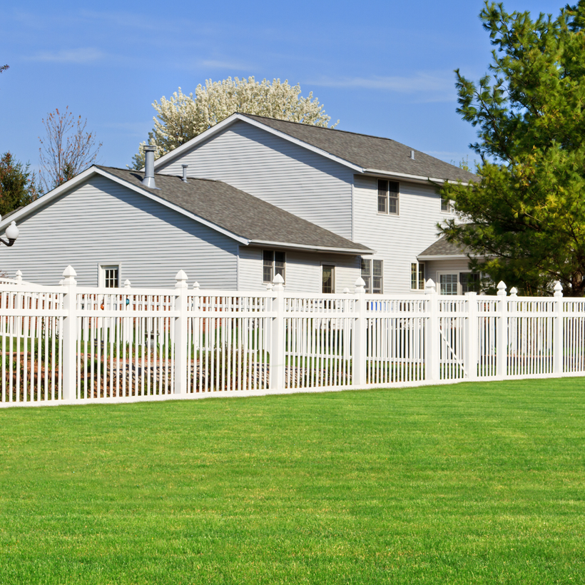 A white fence surrounds a lush green lawn in front of a house.