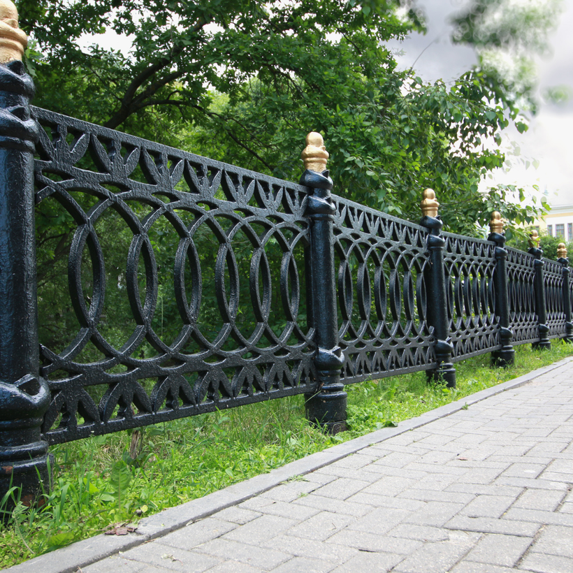 A wrought iron fence along a sidewalk with trees in the background