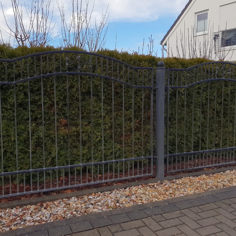 A metal fence surrounds a lush green hedge in front of a house