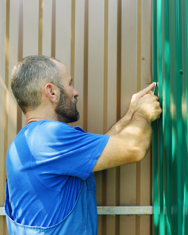 A man in a blue shirt is working on a metal fence.