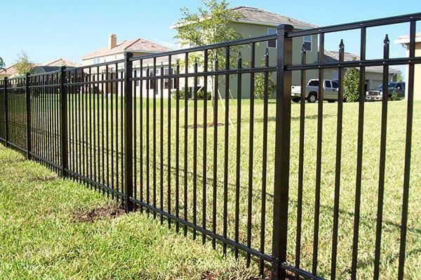 A black wooden fence surrounds a lush green field.