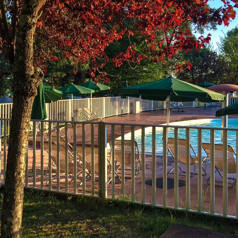 A fence surrounds a swimming pool with chairs and umbrellas