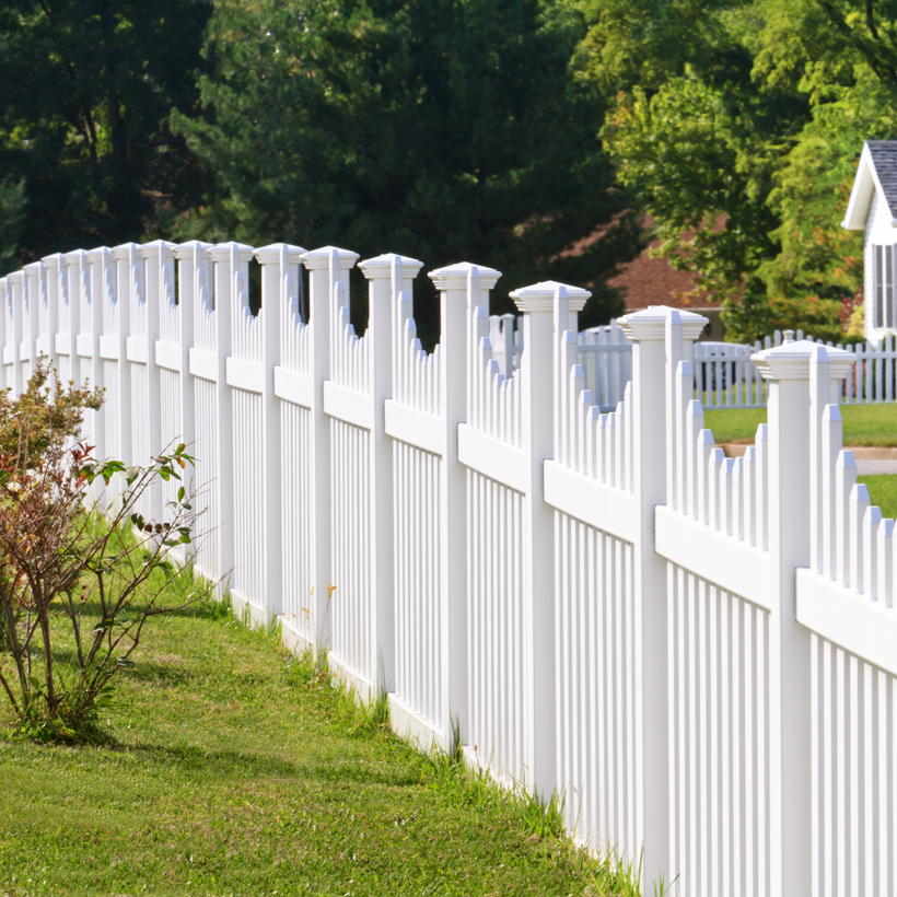 A white fence surrounds a lush green lawn in front of a house.