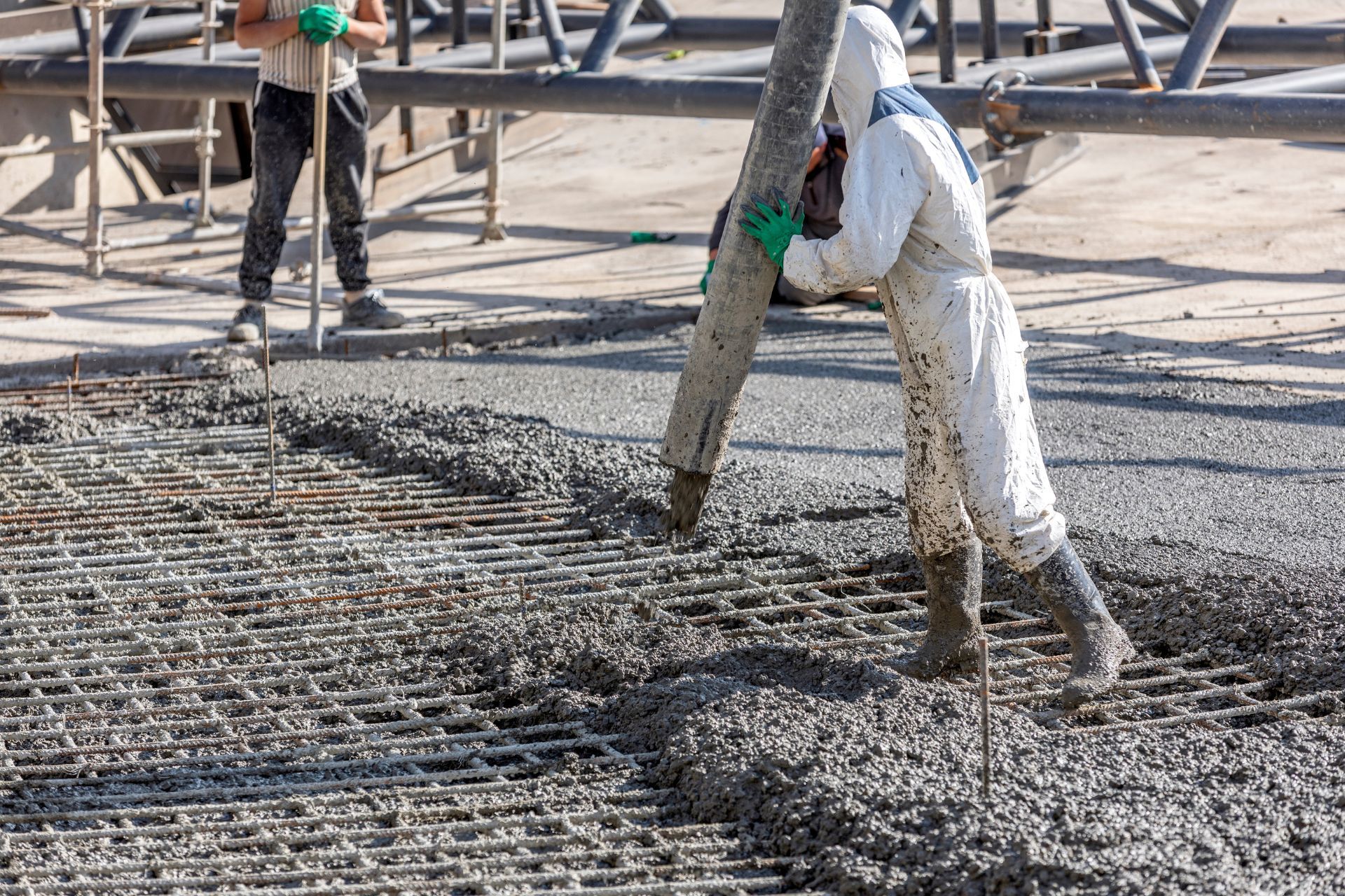 A man is pouring concrete into a grid on a construction site.