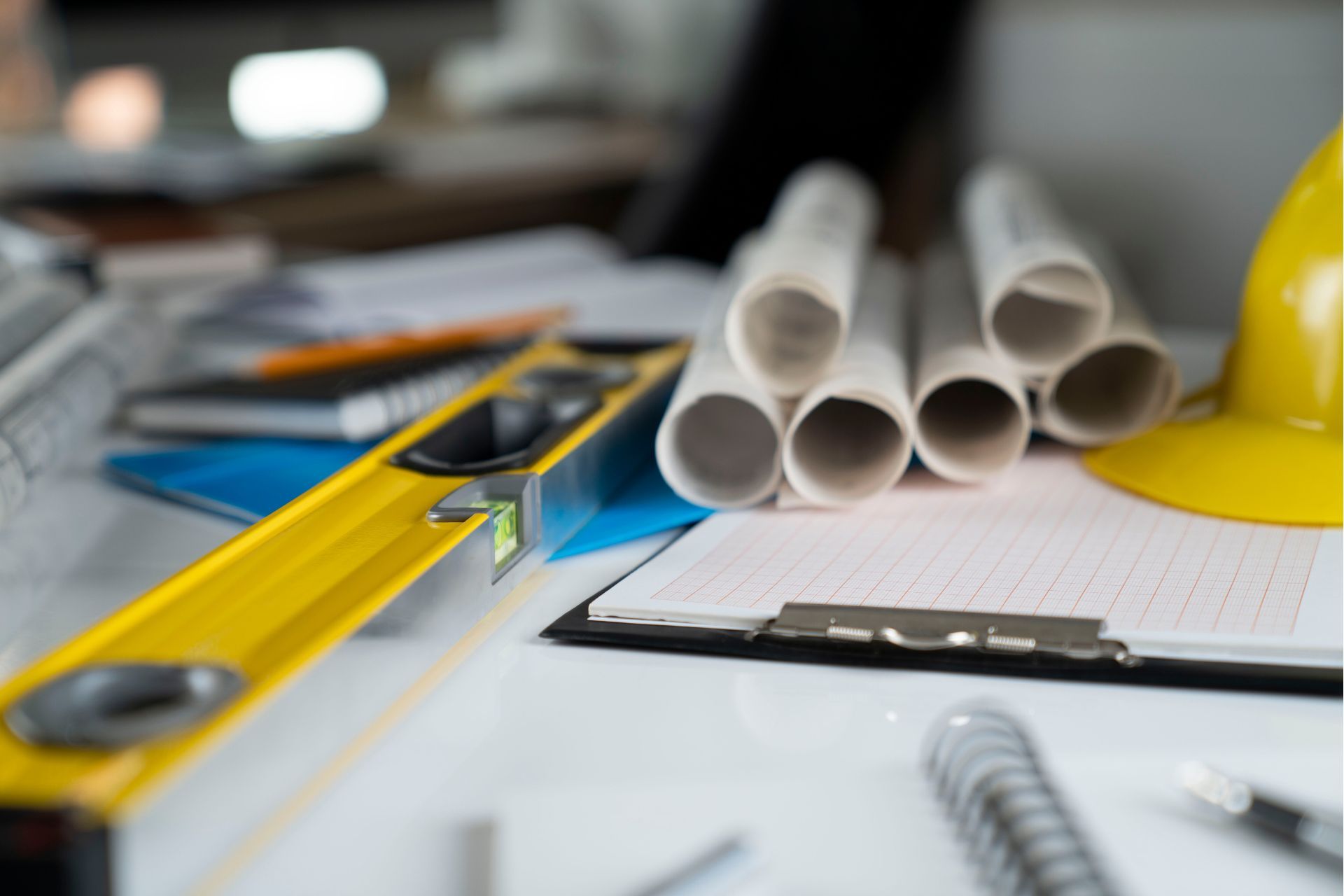 A yellow hard hat is sitting on top of a clipboard next to a level.