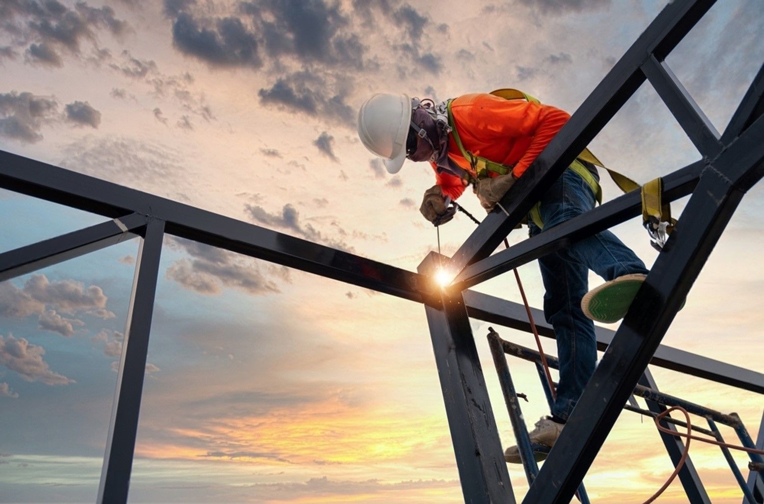 A construction worker is welding a metal structure on a scaffolding.