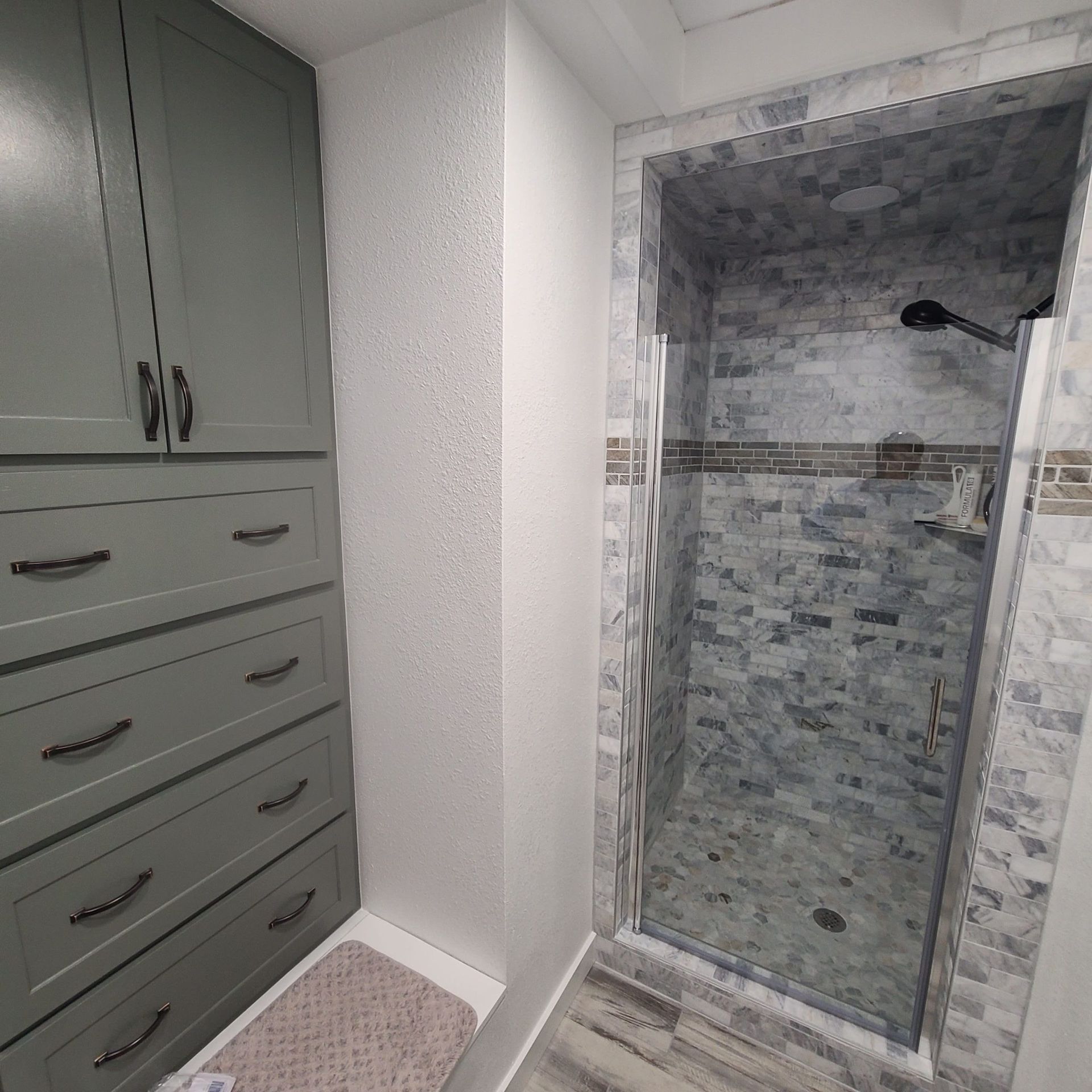 Bathroom with green cabinets, marble-tiled shower, and wood-look floor.