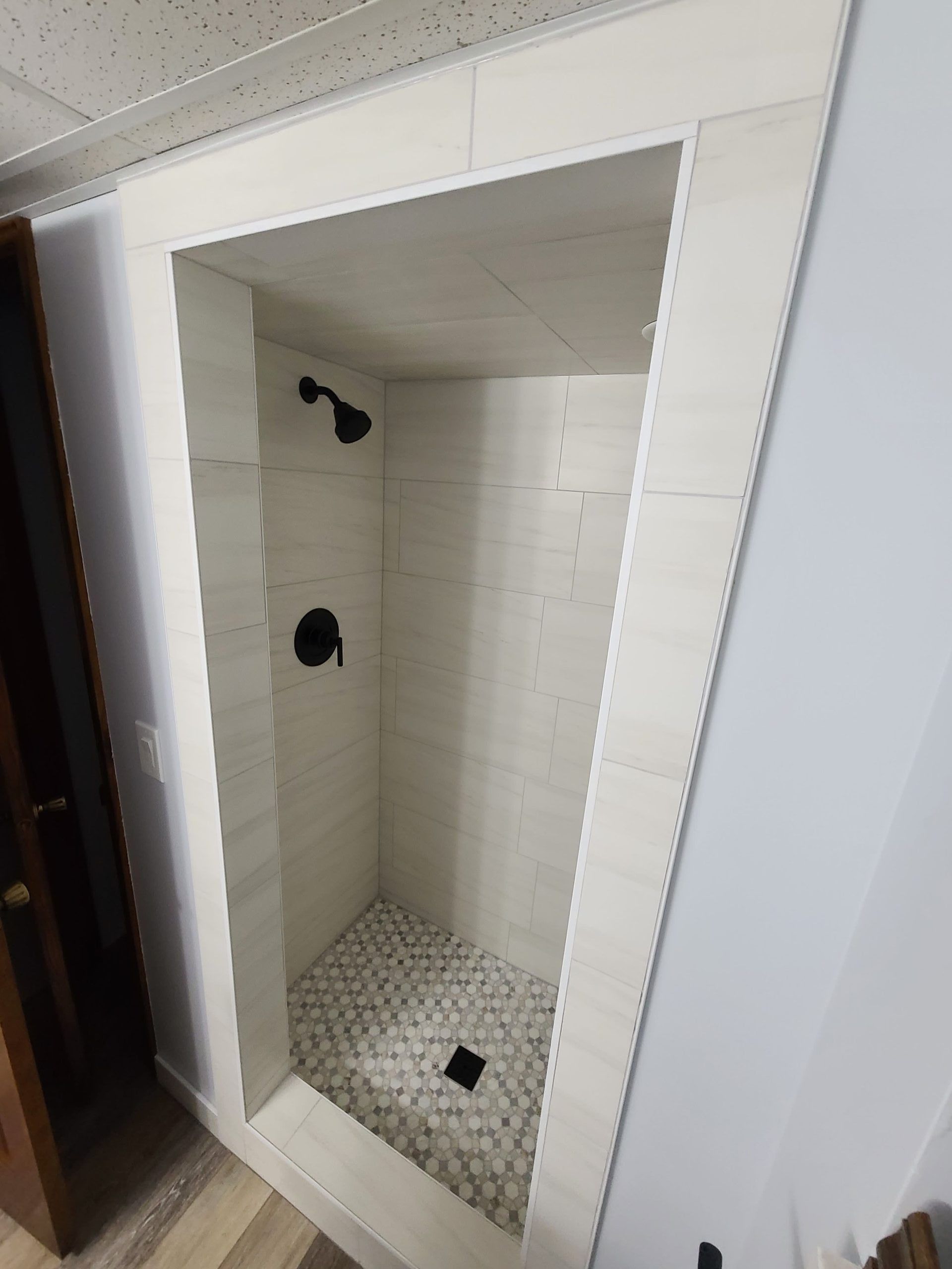 A newly tiled shower stall with black fixtures and a pebble floor, surrounded by light-colored tiles.