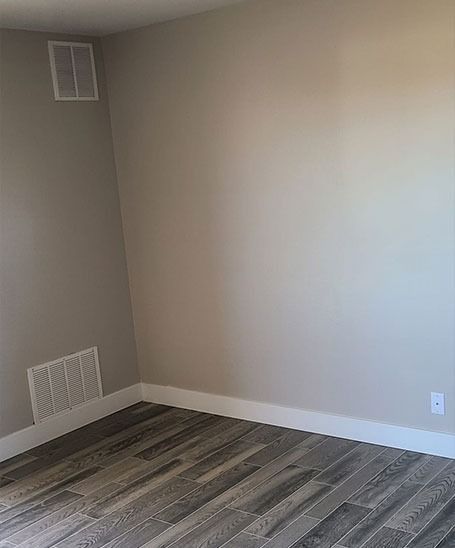 Empty corner of a room with gray walls, white trim, and wood-look flooring.