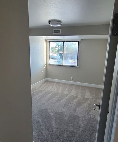 Empty room with gray carpet, window with blinds, and a ceiling light.