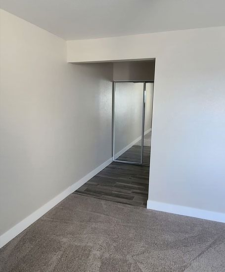Empty room with carpet, wood flooring, and a mirrored closet. Walls are painted beige.