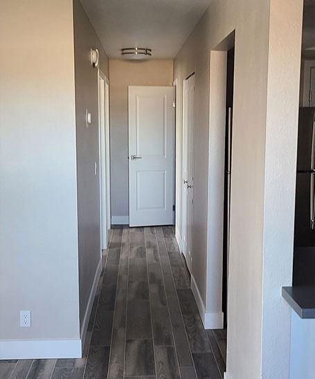 Hallway with wood-look flooring, neutral walls, white doors, and a ceiling light.