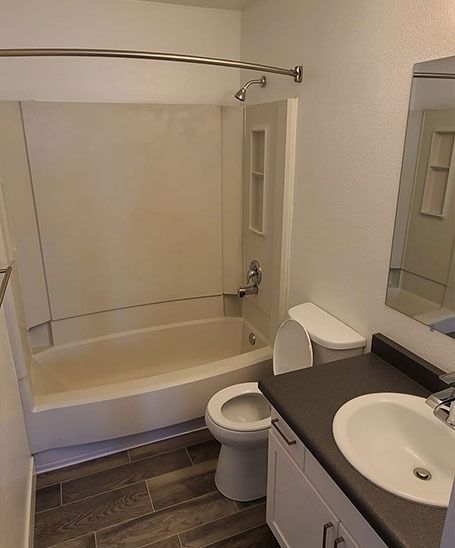 Bathroom with white tub, toilet, and sink, brown tiled floor, and a mirror.