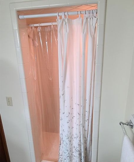 Narrow shower stall with a clear plastic liner and floral-patterned curtain.