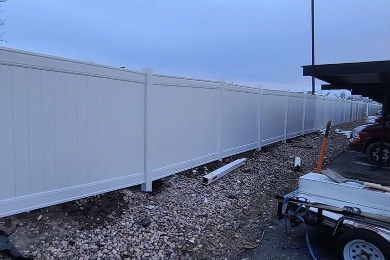 White vinyl fence along a gravel area, under a cloudy sky.