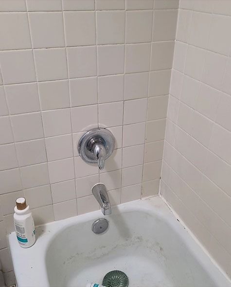 Bathtub with a faucet, showerhead, and a bottle on the side. Cream-colored tile lines the walls.